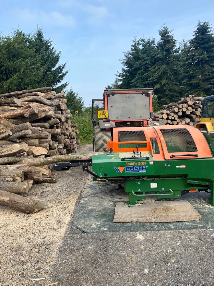 A tractor is parked next to a pile of logs.
